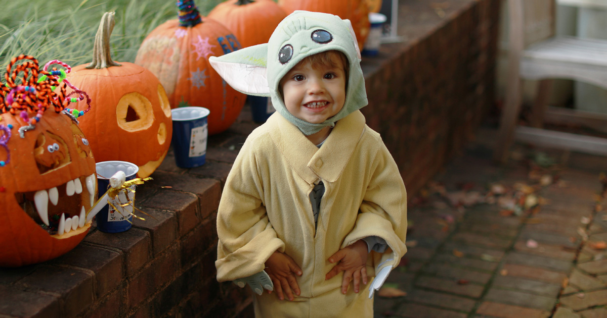 Child in Halloween costume in front of pumpkins