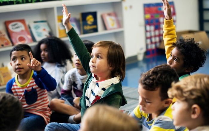 Children sit in class and raise their hands